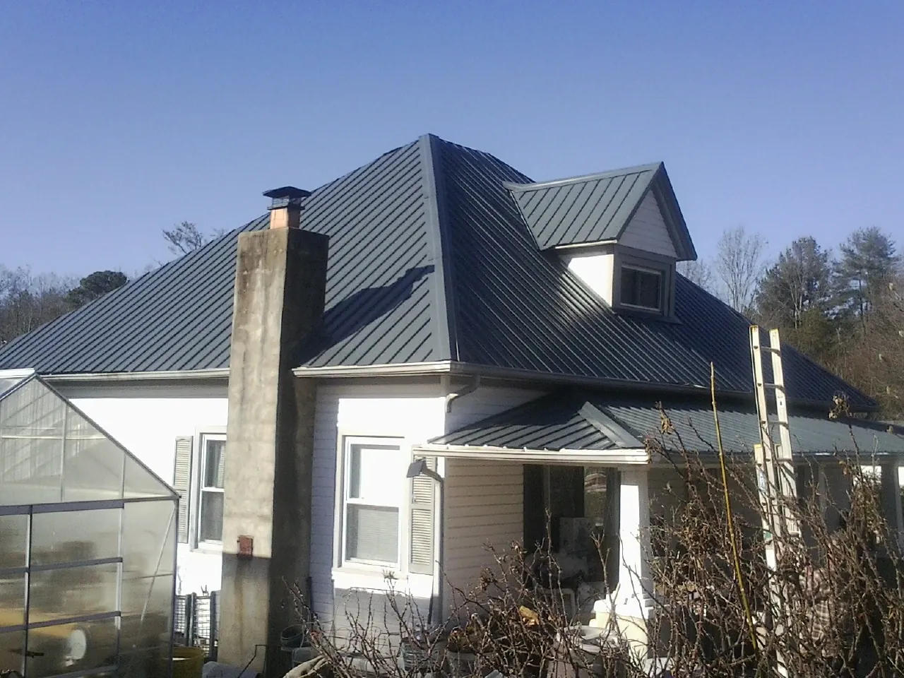 Dark blue standing seam metal roof on a white farmhouse with dormer — Slate & Tile Roof Repair by Roofing Brothers in Saint James