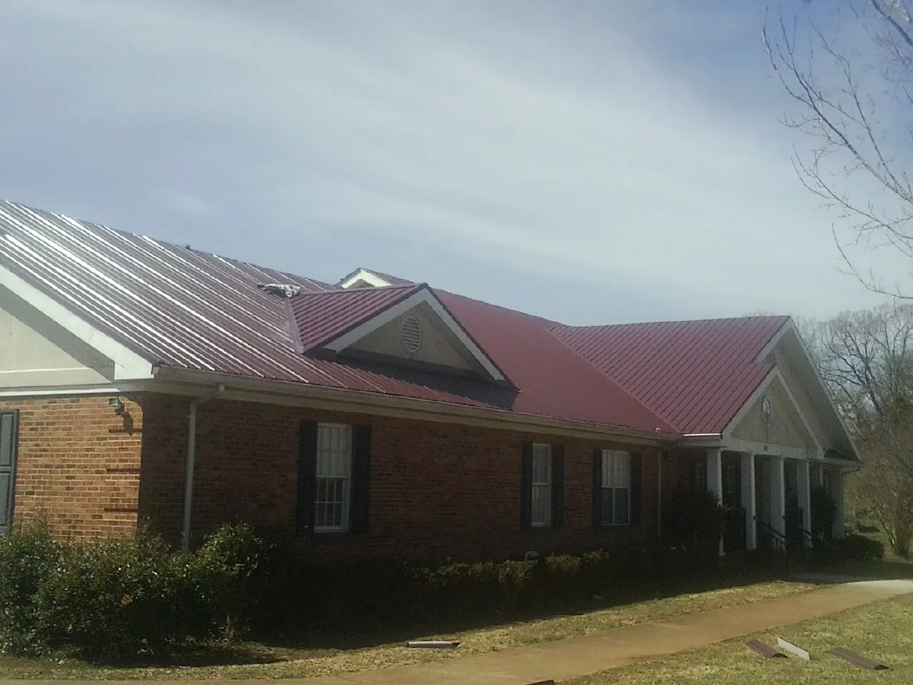 Red metal roof with gabled entries on a long brick building, from a Hail Damage Roof Repair job in Saint James