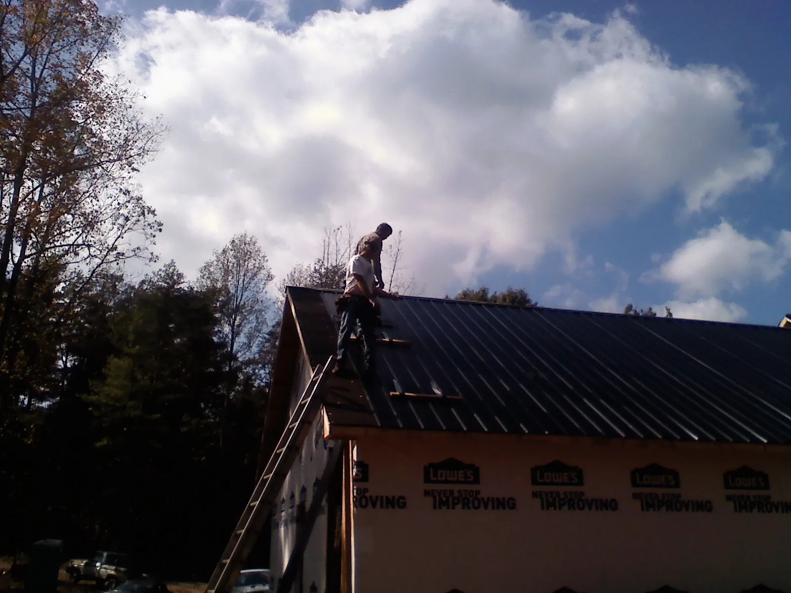 Roofer fastening dark metal panels high against a cloudy sky, from a Roof Inspection job in Saint James