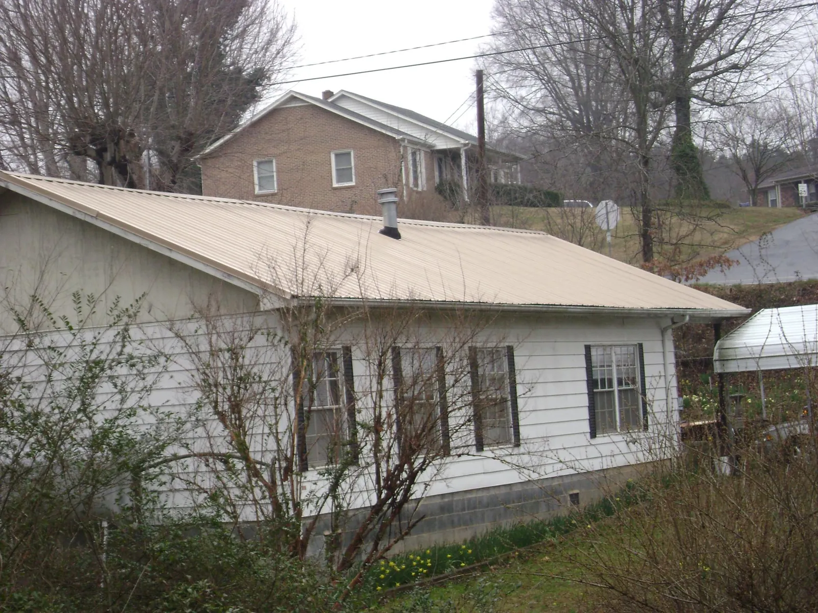 Tan metal roof on a white sided house set into a hillside — Commercial Roofing by Roofing Brothers in Saint James